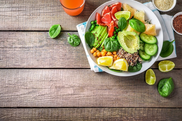 Vegan food concept: quinoa with avocado, cucumbers, green peas, chickpeas, spinach and citrus fruits on wooden background.