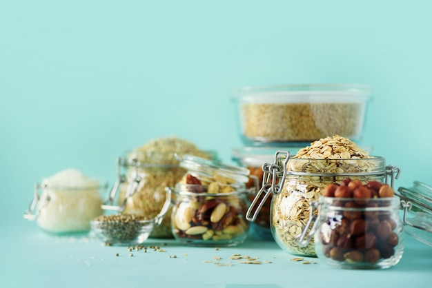 Vegan health food over blue background with copy space. Nuts, seeds, cereals, grains in glass jars. 