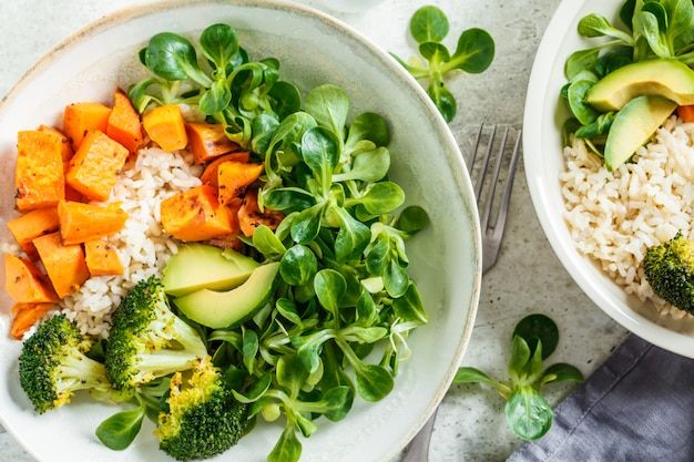 Vegan lunch bowl with rice, broccoli, sweet potato, rice and salad, top view. Vegan food concept.