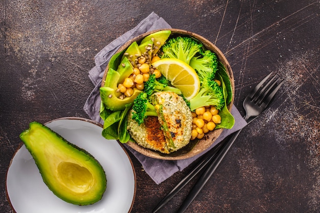 Vegan lunch in a coconut bowl: green burgers with salad and chickpeas. 