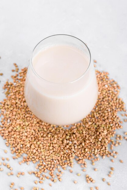 Vegan non diary buckwheat milk in glass with buckwheat groats on a white stone table Vegan buckwheat drink is plant based alternative milk  Veggies healthy milk product close up selective focus