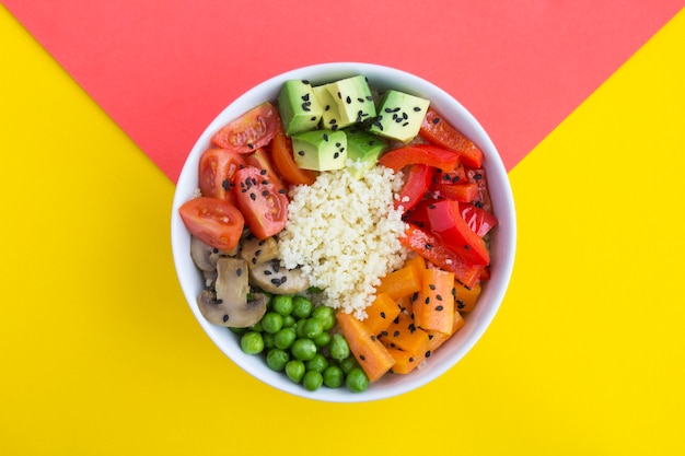 Vegan poke bowl with couscous and vegetables in the white bowl in the center of the bicolor table. Top view. Copy space. Closeup.