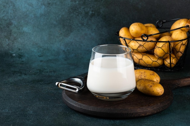 Vegan potato milk in glass and potato in bowl on dark background Vegan milk Plant based milk replacer and lactose free Vegetable milk