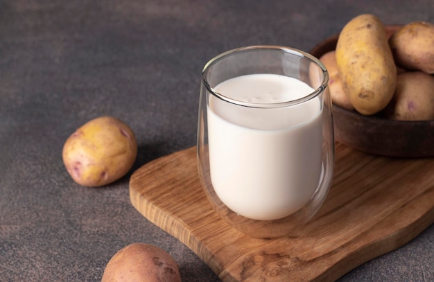 Vegan potato milk in glass and potato in plate on wooden board Plant based milk replacer and lactose free