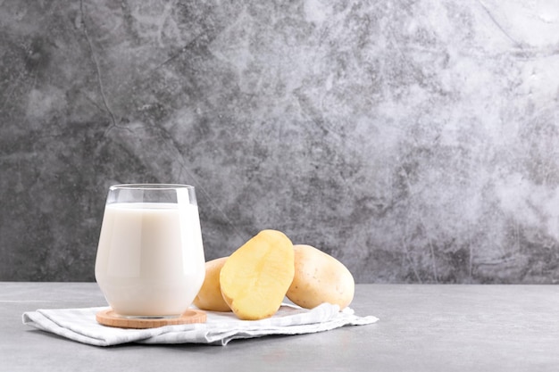 Vegan potato milk in a glass and potato tubers on grey stone table background plant based