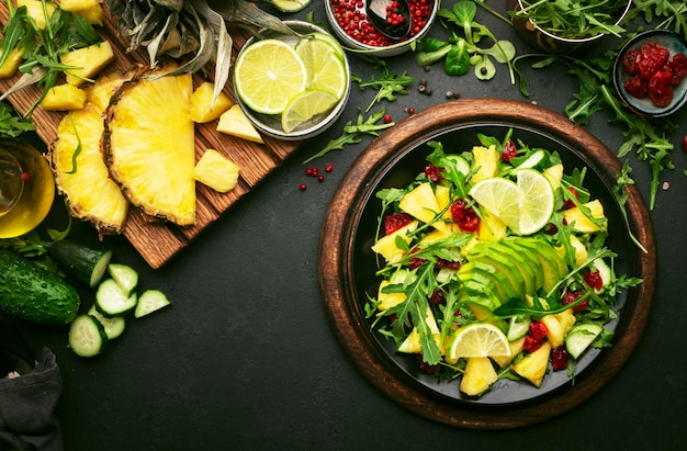 Vegan vegetarian salad with pineapple arugula avocado and dried cherry on black plate on dark stone kitchen table top view Healthy eating clean diet food weight loss concept