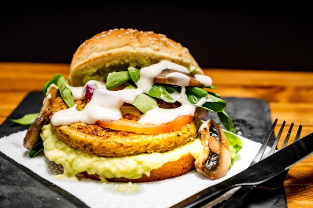 Vegan veggie protein burger with tomato arugula red onion mushrooms and avocado mayonnaise and alioli on a wooden board and a black background Normal view