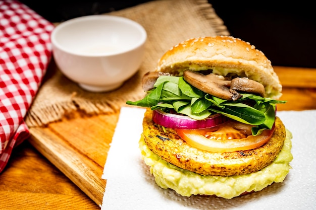 Vegan veggie protein burger with tomato arugula red onion mushrooms and avocado mayonnaise on a wooden board and a black background Chopped view Copy text