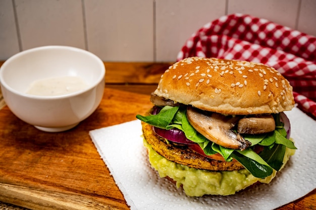 Vegan veggie protein burger with tomato arugula red onion mushrooms and avocado mayonnaise on a wooden board and a white background Chopped view Copy text