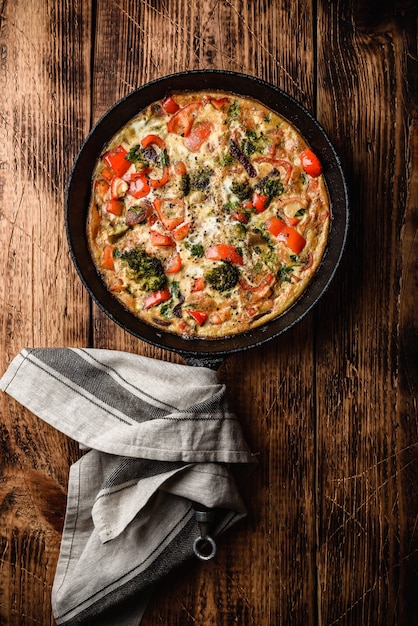 Vegetable frittata with broccoli, red bell pepper and herbs in cast iron skillet. View from above