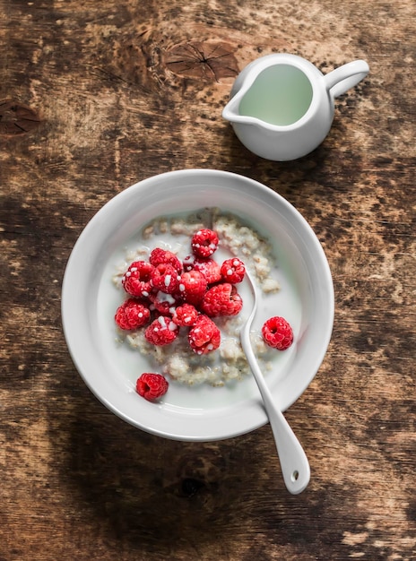 Vegetable milk oatmeal porridge with fresh raspberries on a wooden background top view