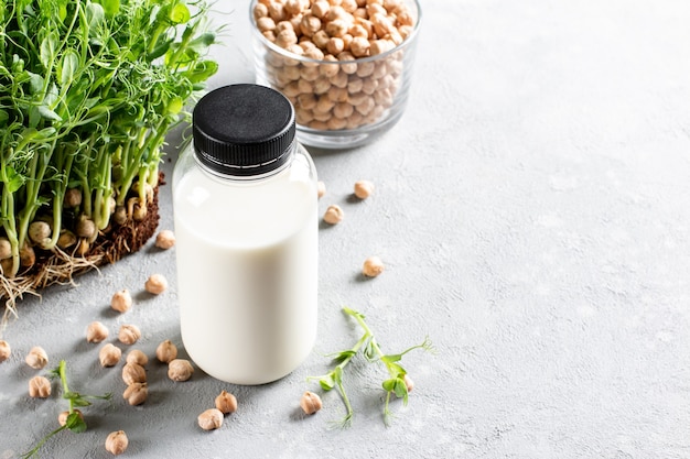 Vegetable pea milk in a bottle and chickpeas on a light gray concrete background