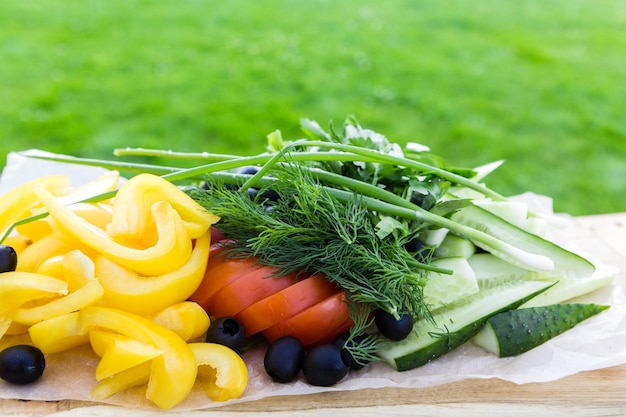 Vegetable plate on a wooden dish against the background of bright green grass Healthy food concept Horizontal photo