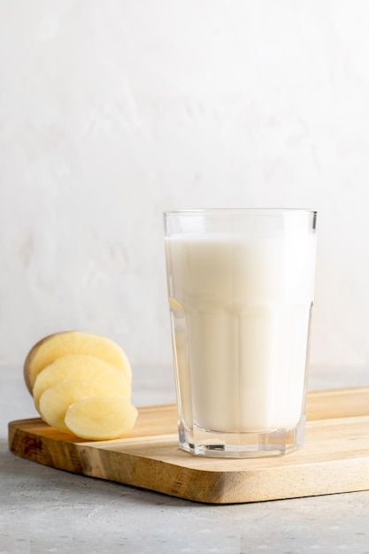 Vegetable potato milk in glass potato purified tuber on wooden kitchen board on neutral backdrop