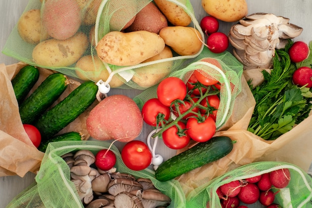 Vegetable in reusable bags on wood background, top view