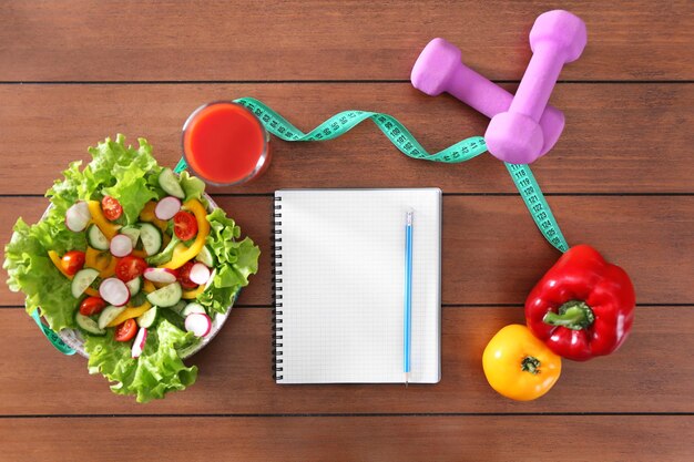 Vegetable salad and blank notebook on wooden table top view