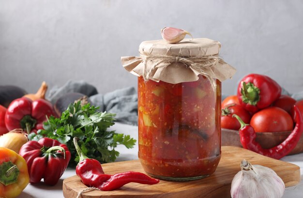 Vegetable salad with eggplant, carrot, peppers, onion and tomatoes in glass jar on wooden board