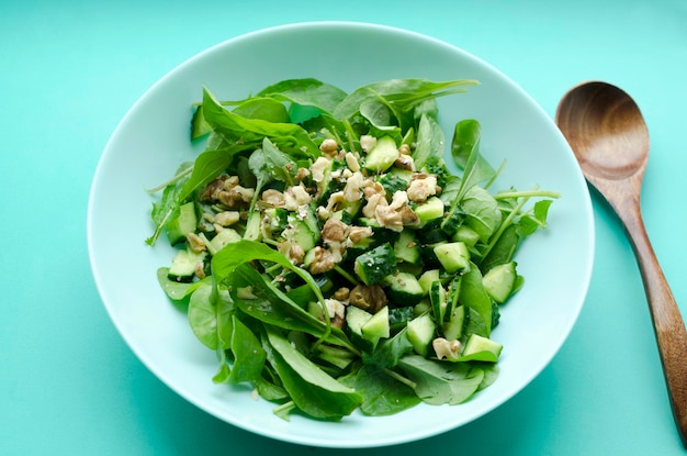 Vegetable salad with fresh arugula cucumber in a plate with wooden spoon on turquoise background cl