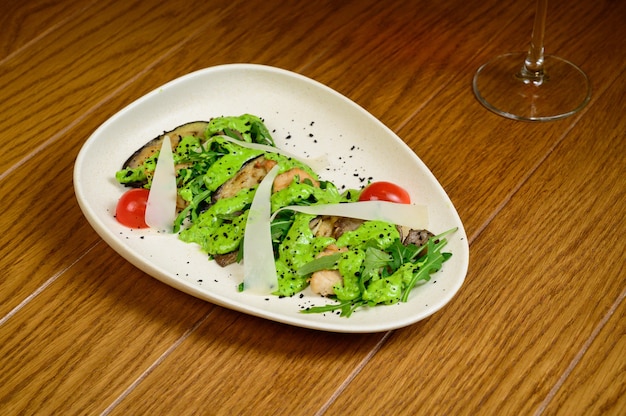 Vegetable salad with fried eggplant on white plate on wooden background