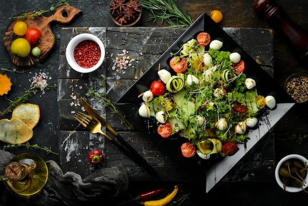 Vegetable salad with mozzarella cheese. On a black plate. Top view. Food. Rustic style.