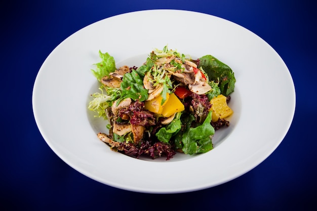 Vegetable salad with mushrooms, bell peppers, onions, lettuce and sauce with mustard seeds. Flat lay top view on a white plate on a blue background.