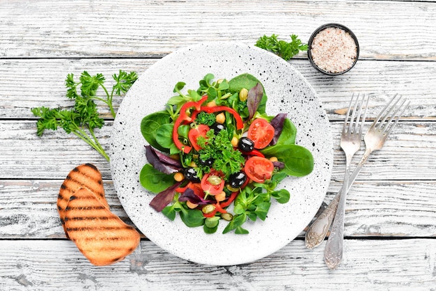 Vegetable salad with spinach tomatoes paprika and pumpkin seeds in a plate on a wooden background Top view Free space for your text Flat lay