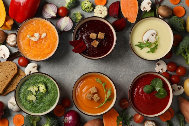 Vegetable soups and ingredients on grey, top view