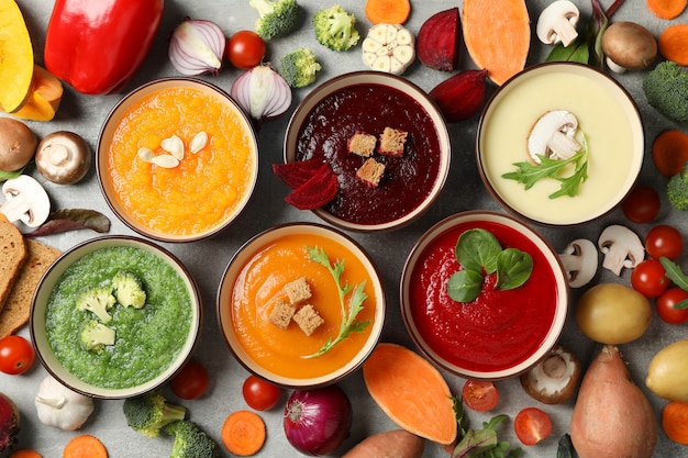 Vegetable soups and ingredients on grey, top view