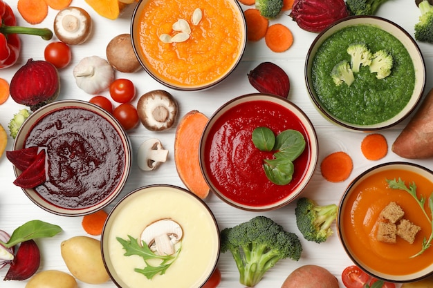 Vegetable soups and ingredients on white wooden, top view