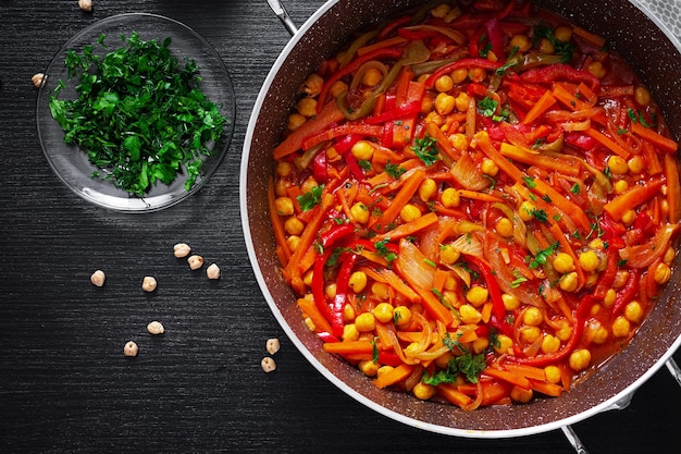 Vegetable stew of chickpeas carrot sweet peppers onions garlic and tomato sauce with lemon on the dark table Oriental cuisine Top view