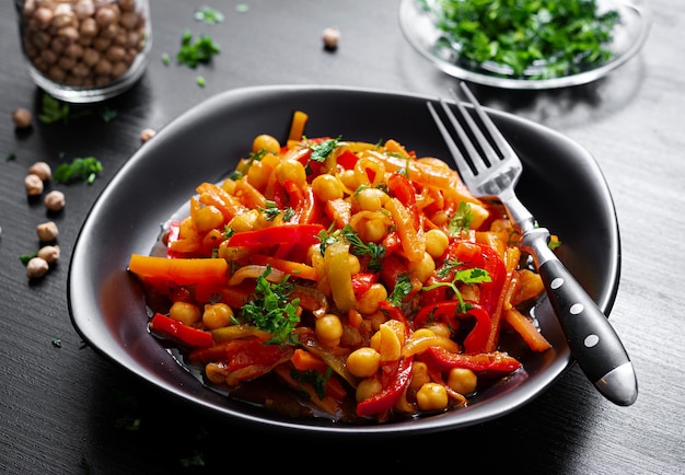 Vegetable stew of chickpeas carrot sweet peppers onions garlic and tomato sauce with lemon on the dark table Oriental cuisine