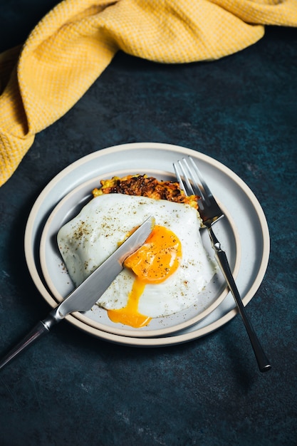 Photo vegetable zucchini and carrot fritters and an egg with a runny yolk on top, served on a blue plate, knife and fork, yellow towel,