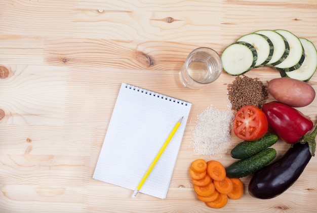 Vegetables and cereals and notebook on a wooden table