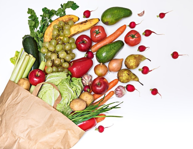 Vegetables and fruits in abundance spill out of a paper bag isolated on a white background Delivery and purchase of healthy eco food enriched with vitamins and fiber