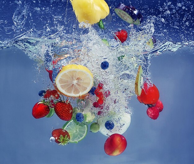 Vegetables and fruits falling into water on color background