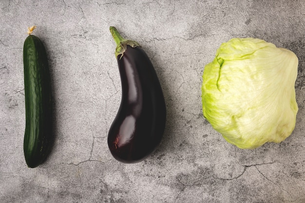 Vegetables on a gray background: lettuce leaves, cucumber and eggplant, top view