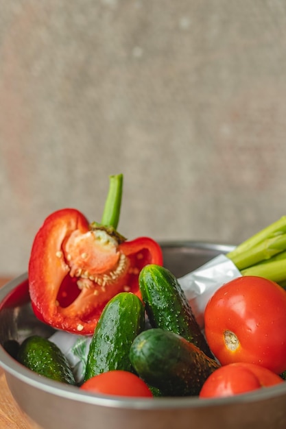 Vegetables lie in a metal bowl tomatoes asparagus cucumbers red bell peppers on a wooden board and brown background back gray background place for text