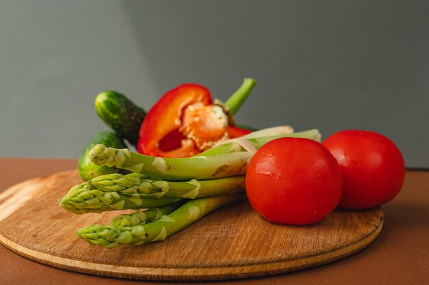 Vegetables lie on a wooden board tomatoes asparagus cucumbers red bell peppers brown dark gray background place for text