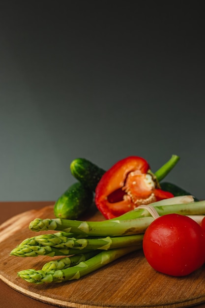 Vegetables lie on a wooden board tomatoes asparagus cucumbers red bell peppers brown dark gray background place for text