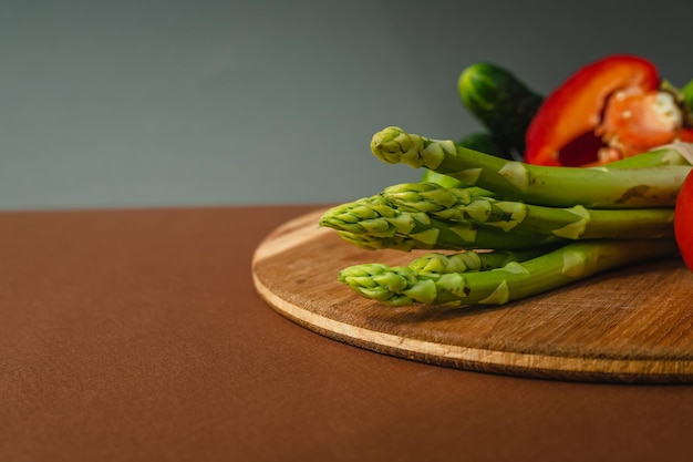 Vegetables lie on a wooden board tomatoes asparagus cucumbers red bell peppers brown dark gray background place for text