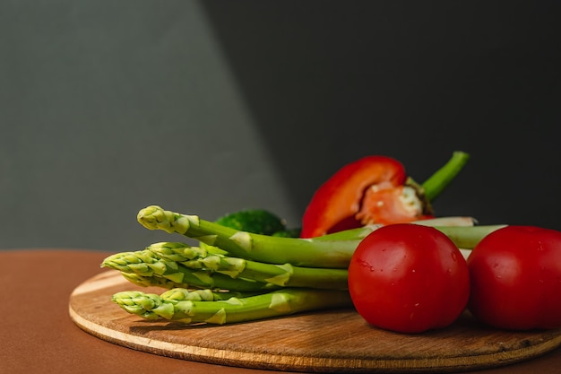 Vegetables lie on a wooden board tomatoes asparagus cucumbers red bell peppers brown dark gray background place for text