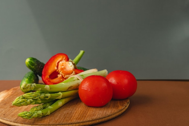 Vegetables lie on a wooden board tomatoes asparagus cucumbers red bell peppers brown dark gray background place for text