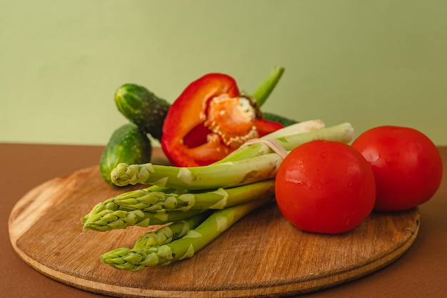 Vegetables lie on a wooden board tomatoes asparagus cucumbers red bell peppers brown light green background place for text