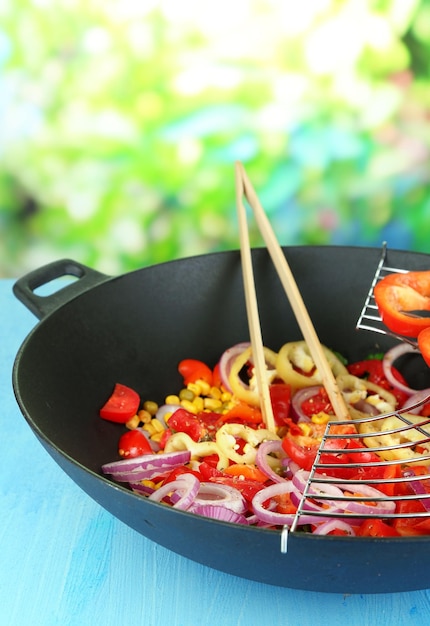 Vegetables in wok on wooden table on natural background