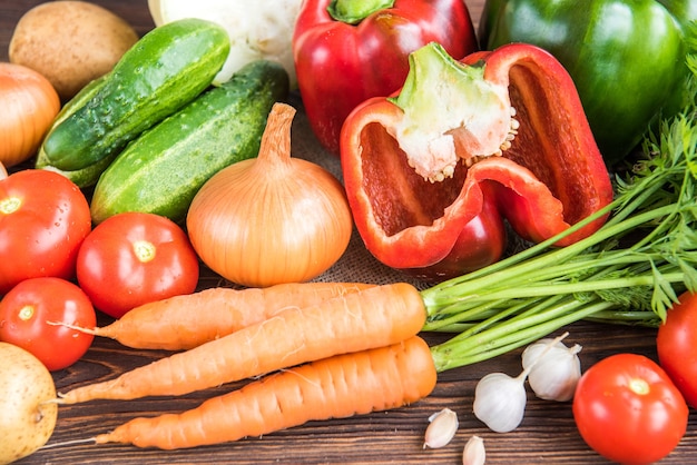 Vegetables on wooden background. Carrot, red pepper, cucumbers, tomatoes, garlic, potatoes and onions.