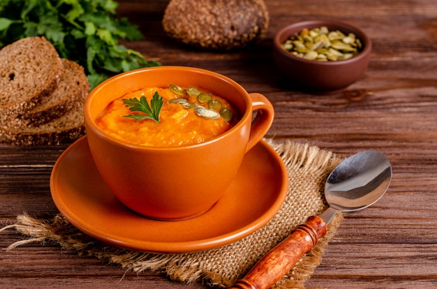 Vegetarian autumn cream soup of pumpkins and carrots with seeds and parsley on a wooden surface with copy space, flat lay