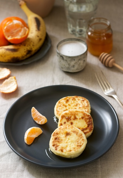 Vegetarian breakfast of quark pancakes with honey, fruit and coffee with milk. Rustic style.