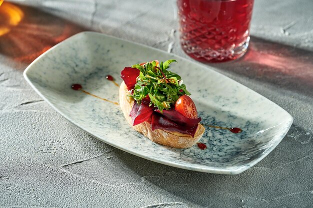 Vegetarian bruschetta with beets tomatoes and arugula in a plate on a concrete background