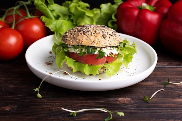 Vegetarian burger with green, red vegetables and micro grins on a white plate on a dark wooden table, close up.