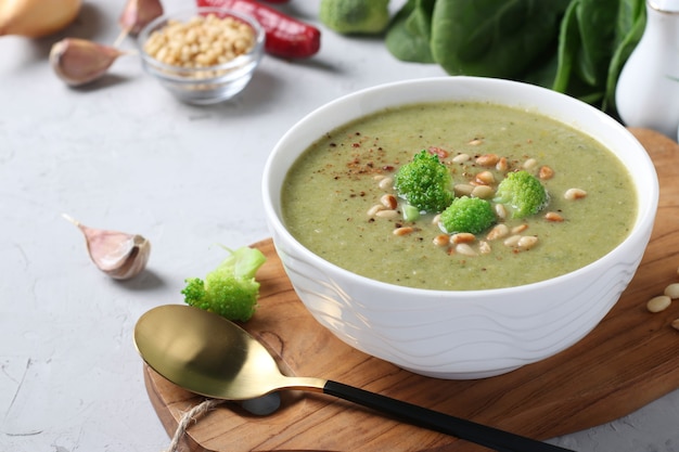 Vegetarian cream soup with broccoli, spinach and zucchini in white bowl on gray background. 